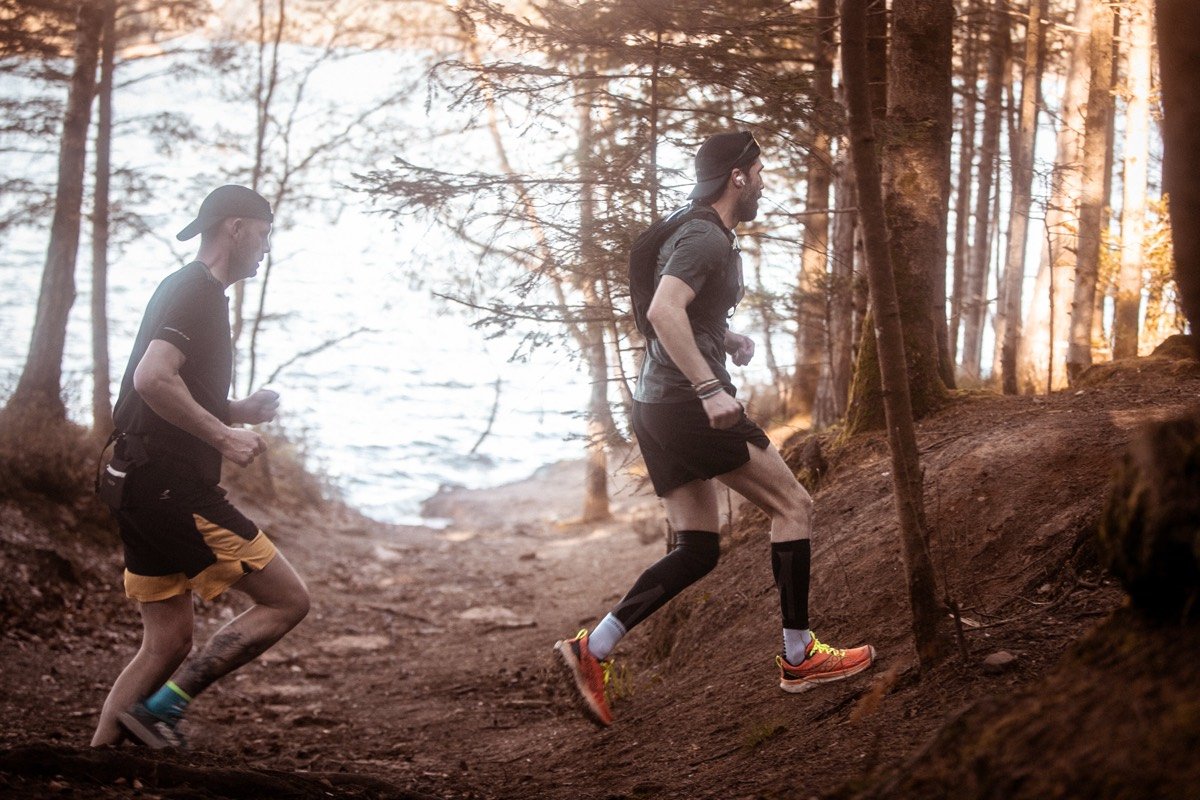 Deux coureurs en sous-bois, le lac en contre-jour